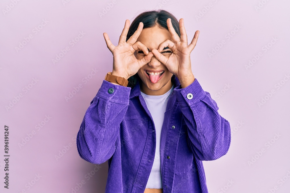 Young brunette woman wearing casual clothes doing ok gesture like binoculars sticking tongue out, eyes looking through fingers. crazy expression. Young brunette woman wearing casual clothes doing ok gesture like binoculars sticking tongue out, eyes looking through fingers. crazy expression.
