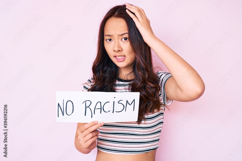 Young beautiful chinese girl holding no racism banner stressed and frustrated with hand on head, surprised and angry face Young beautiful chinese girl holding no racism banner stressed and frustrated with hand on head, surprised and angry face