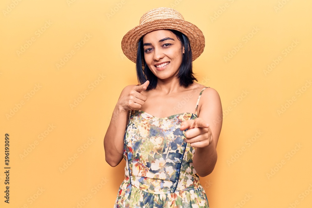 Young beautiful latin woman wearing summer hat pointing fingers to camera with happy and funny face. good energy and vibes. Young beautiful latin woman wearing summer hat pointing fingers to camera with happy and funny face. good energy and vibes.