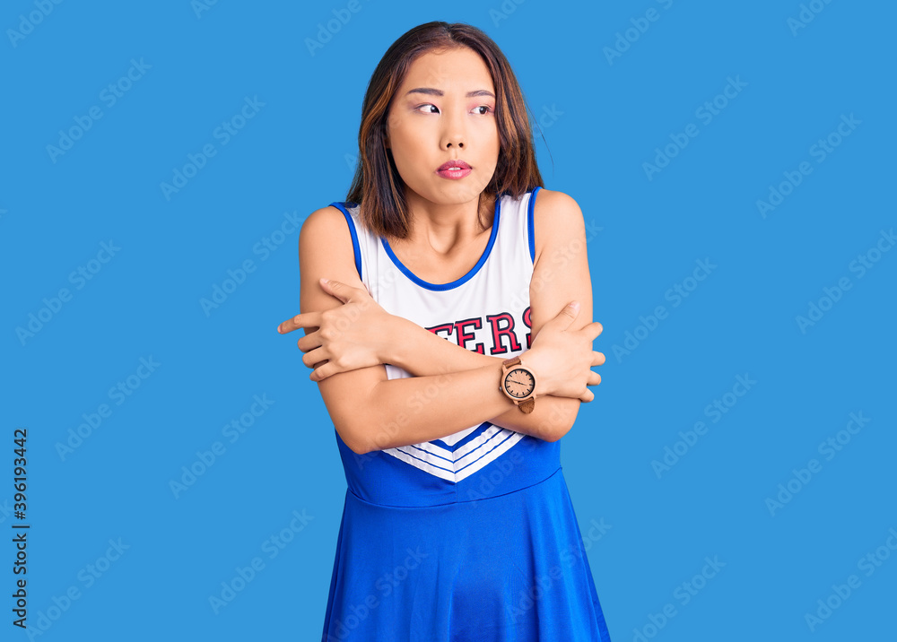 Young beautiful chinese girl wearing cheerleader uniform shaking and freezing for winter cold with sad and shock expression on face Young beautiful chinese girl wearing cheerleader uniform shaking and freezing for winter cold with sad and shock expression on face