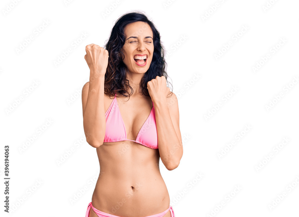 Young beautiful hispanic woman wearing bikini celebrating surprised and amazed for success with arms raised and eyes closed. winner concept. Young beautiful hispanic woman wearing bikini celebrating surprised and amazed for success with arms raised and eyes closed. winner concept.