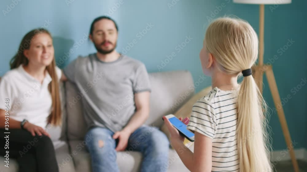Small beautiful girl is playing interactive game at home, holding her gadget, looking on a screen and explaining words using gestures, while parents are guessing, all enjoy family time, Slow motion. Small beautiful girl is playing interactive game at home, holding her gadget, looking on a screen and explaining words using gestures, while parents are guessing, all enjoy family time, Slow motion.