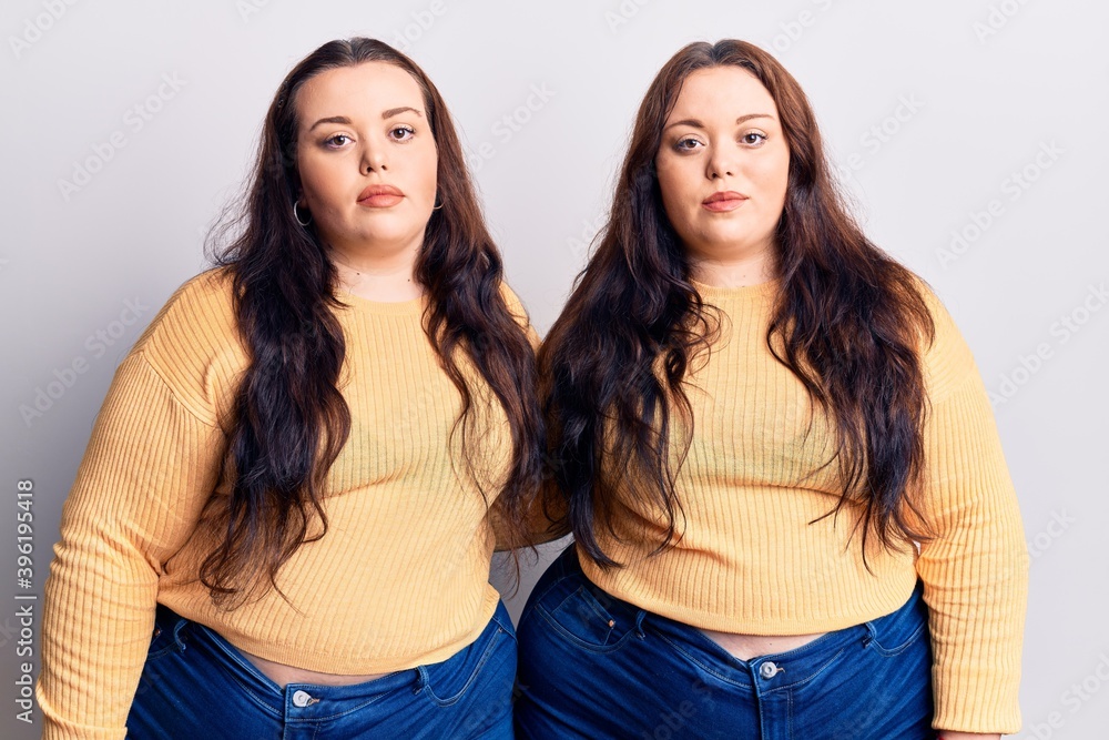 Young plus size twins wearing casual clothes relaxed with serious expression on face. simple and natural looking at the camera. Young plus size twins wearing casual clothes relaxed with serious expression on face. simple and natural looking at the camera.