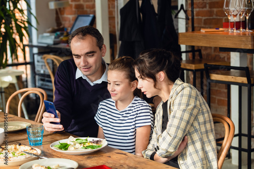 Family  parenthood  communication and people concept - happy mother  father and their girl having dinner and talking at a restaurant or cafe.