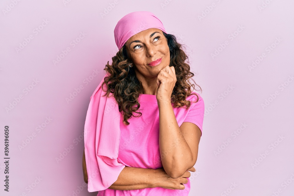 Middle age hispanic woman wearing breast cancer support pink scarf serious face thinking about question with hand on chin, thoughtful about confusing idea Middle age hispanic woman wearing breast cancer support pink scarf serious face thinking about question with hand on chin, thoughtful about confusing idea