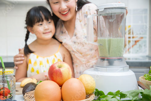 Happy asian family mother and her daughter enjoy prepare freshly squeezed fruits with vegetables for making smoothies for breakfast together in the kitchen.diet and Health concept.