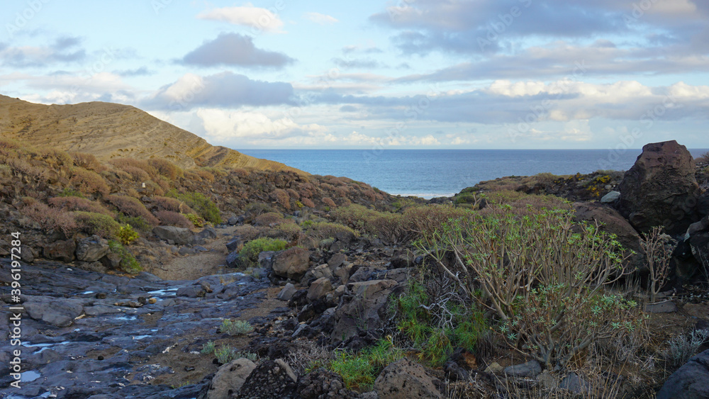Hike path between volcanic rocks leading to the ocean in El Medano, Tenerife, Canary Islands, Spain     