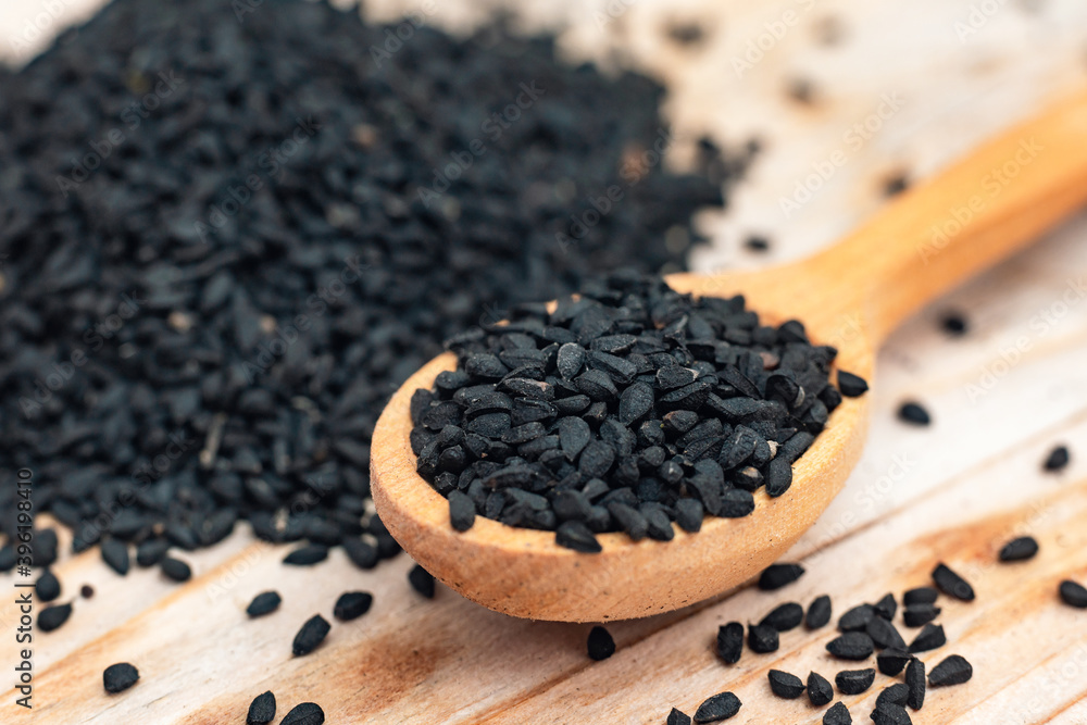 Black cumin seeds on wooden spoon on wooden background Black cumin seeds on wooden spoon on wooden background