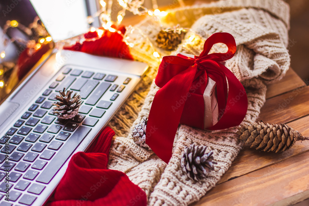 Fototapeta premium Gift with a red bow and laptop Christmas cones and a light knitted scarf Christmas online shopping
