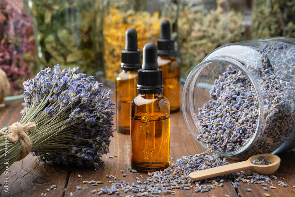 Dropper bottle of lavender essential oil, glass jar of dry lavender flowers,  bunches of dry lavender. Jars of different dry medicinal herbs on  background. Alternative medicine. Stock Photo