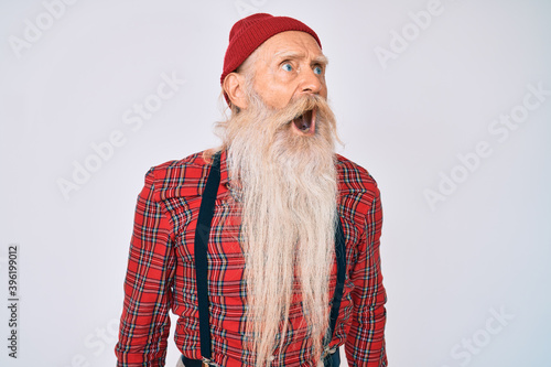 Old senior man with grey hair and long beard wearing hipster look with wool cap angry and mad screaming frustrated and furious, shouting with anger. rage and aggressive concept.