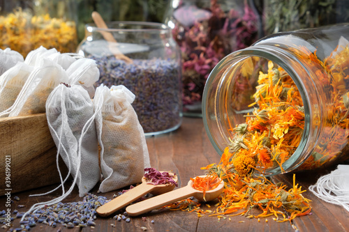 Filter tea bags filled with medicinal herbs. Glass jar of dry calendula flowers for making herbal tea, jars of various healthy herbs on table. Alternative medicine.