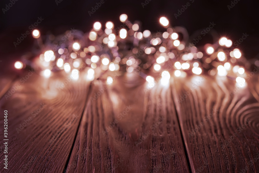 Blured shining christmas lights garland on a dark wood tabletop. Glowing LED lightning decorations in a darkness. Winter season holidays Christmas and New Year. Copy space.