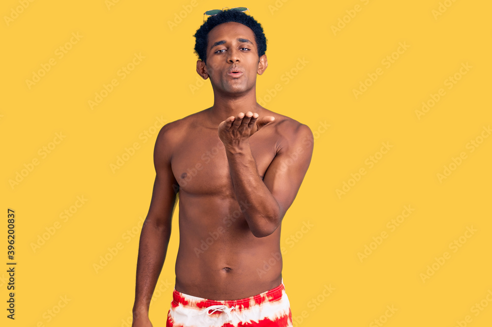 Fototapeta premium African handsome man wearing swimsuit and sunglasses looking at the camera blowing a kiss with hand on air being lovely and sexy. love expression.