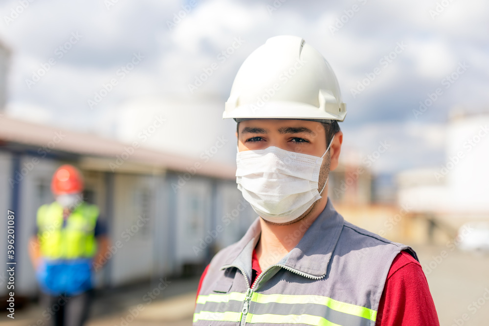 Worker is using a protective face mask for coronavirus and looking at the camera in the construction site. The group of viruses cause respiratory tract infections that can range from mild to lethal. Worker is using a protective face mask for coronavirus and looking at the camera in the construction site. The group of viruses cause respiratory tract infections that can range from mild to lethal.