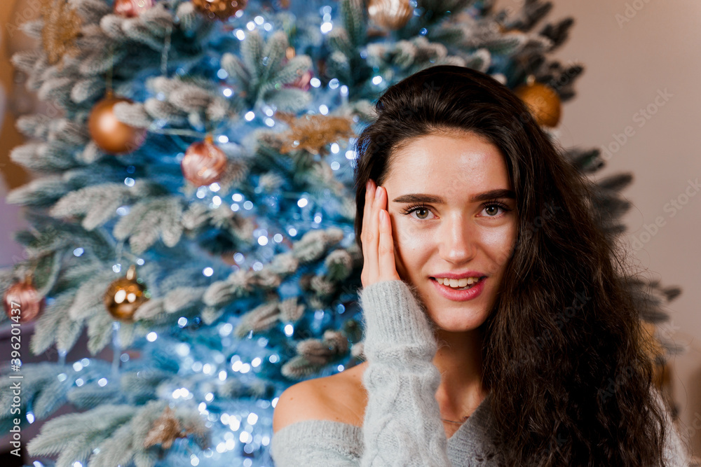 Girl near the Christmas tree smiling and posing. Seasonal advertising before the new year. Celebrating christmas at home