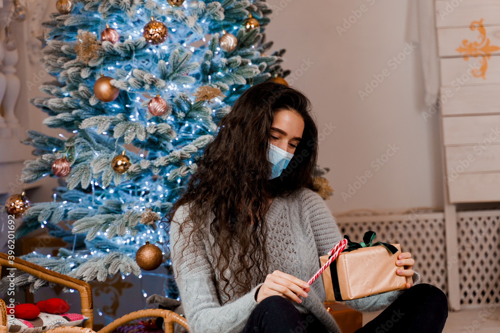 Girl in a medical mask with a Christmas present and candy. celebration of the new year on self-isolation. Pandemic coronavirus covid-19 concept. Advertising sale during the quarantine period Girl in a medical mask with a Christmas present and candy. celebration of the new year on self-isolation. Pandemic coronavirus covid-19 concept. Advertising sale during the quarantine period