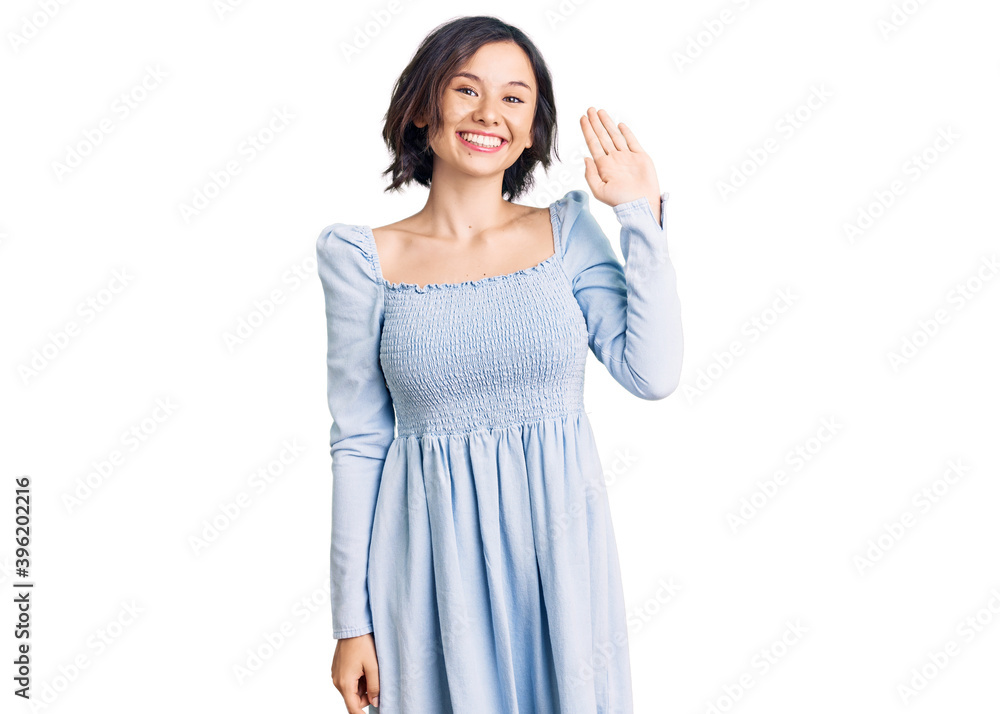 Young beautiful girl wearing casual clothes waiving saying hello happy and smiling, friendly welcome gesture Young beautiful girl wearing casual clothes waiving saying hello happy and smiling, friendly welcome gesture