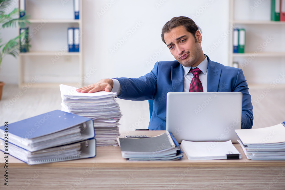 Young male employee unhappy with excessive work in the office Young male employee unhappy with excessive work in the office