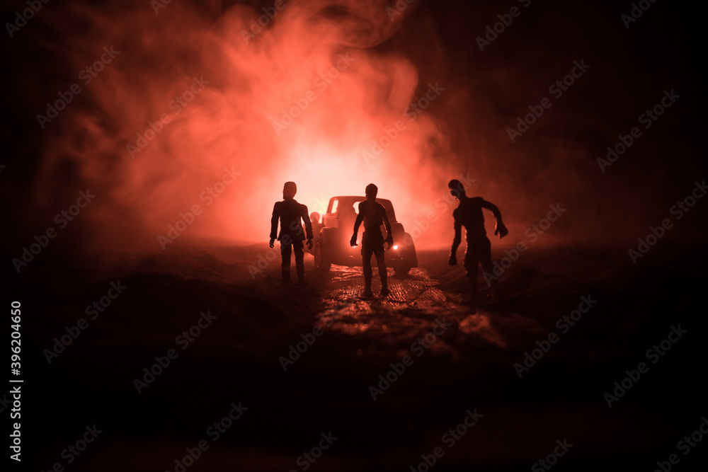 photo of a car stopped on the road lighting up a zombies. Silhouette terrible zombie night near the car. Miniature decoration.