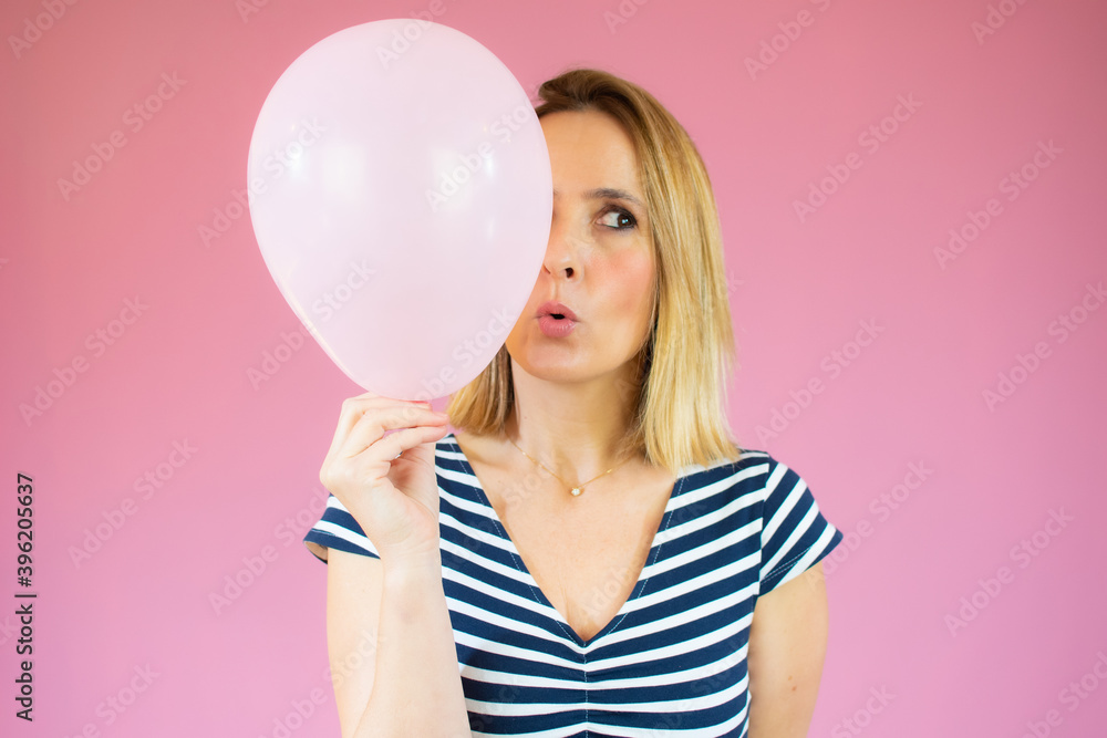 Young happy woman in striped t-shirt , holding one balloon, ready for fancy party, isolated on pink background Young happy woman in striped t-shirt , holding one balloon, ready for fancy party, isolated on pink background