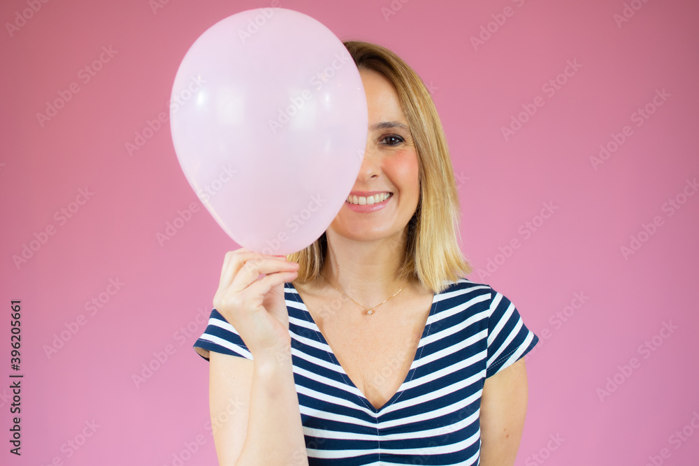 Young happy woman in striped t-shirt , holding one balloon, ready for fancy party, isolated on pink background Young happy woman in striped t-shirt , holding one balloon, ready for fancy party, isolated on pink background