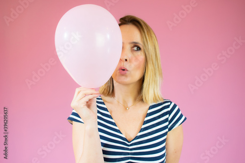 Young happy woman in striped t-shirt , holding one balloon, ready for fancy party, isolated on pink background
