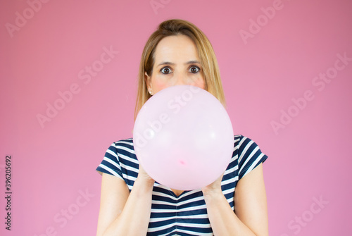 Young happy woman in striped t-shirt , holding one balloon, ready for fancy party, isolated on pink background © Danko