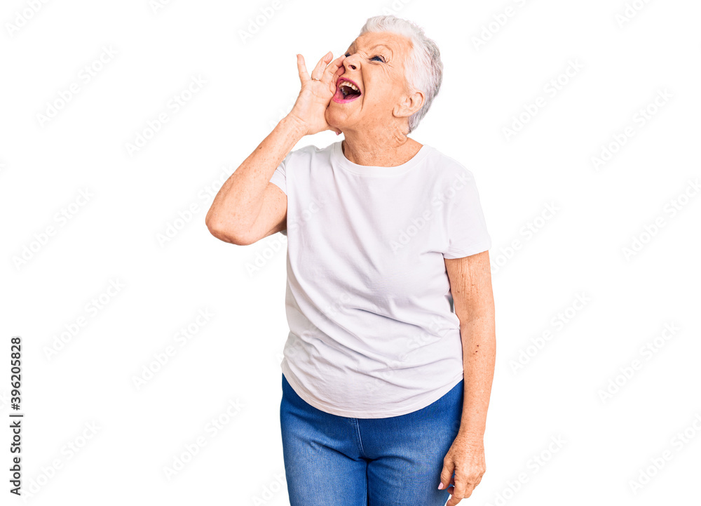 Senior beautiful woman with blue eyes and grey hair wearing casual white tshirt shouting and screaming loud to side with hand on mouth. communication concept. Senior beautiful woman with blue eyes and grey hair wearing casual white tshirt shouting and screaming loud to side with hand on mouth. communication concept.