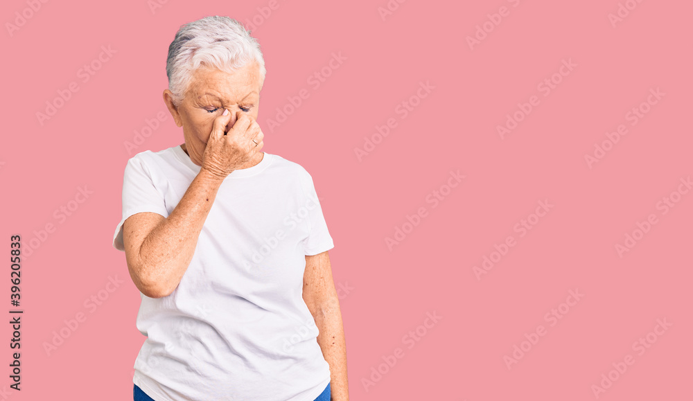 Senior beautiful woman with blue eyes and grey hair wearing casual white tshirt tired rubbing nose and eyes feeling fatigue and headache. stress and frustration concept. Senior beautiful woman with blue eyes and grey hair wearing casual white tshirt tired rubbing nose and eyes feeling fatigue and headache. stress and frustration concept.