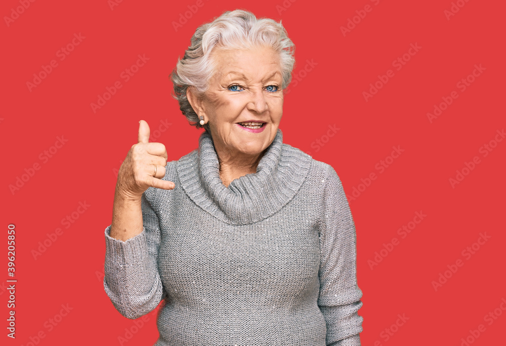 Senior grey-haired woman wearing casual winter sweater smiling doing phone gesture with hand and fingers like talking on the telephone. communicating concepts. Senior grey-haired woman wearing casual winter sweater smiling doing phone gesture with hand and fingers like talking on the telephone. communicating concepts.