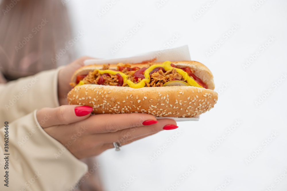 woman holds fresh hot dog in hands, closeup. Hot dog with twhich sausage, grilled onion, mustard, ketchup, pickle cucumbers woman holds fresh hot dog in hands, closeup. Hot dog with twhich sausage, grilled onion, mustard, ketchup, pickle cucumbers