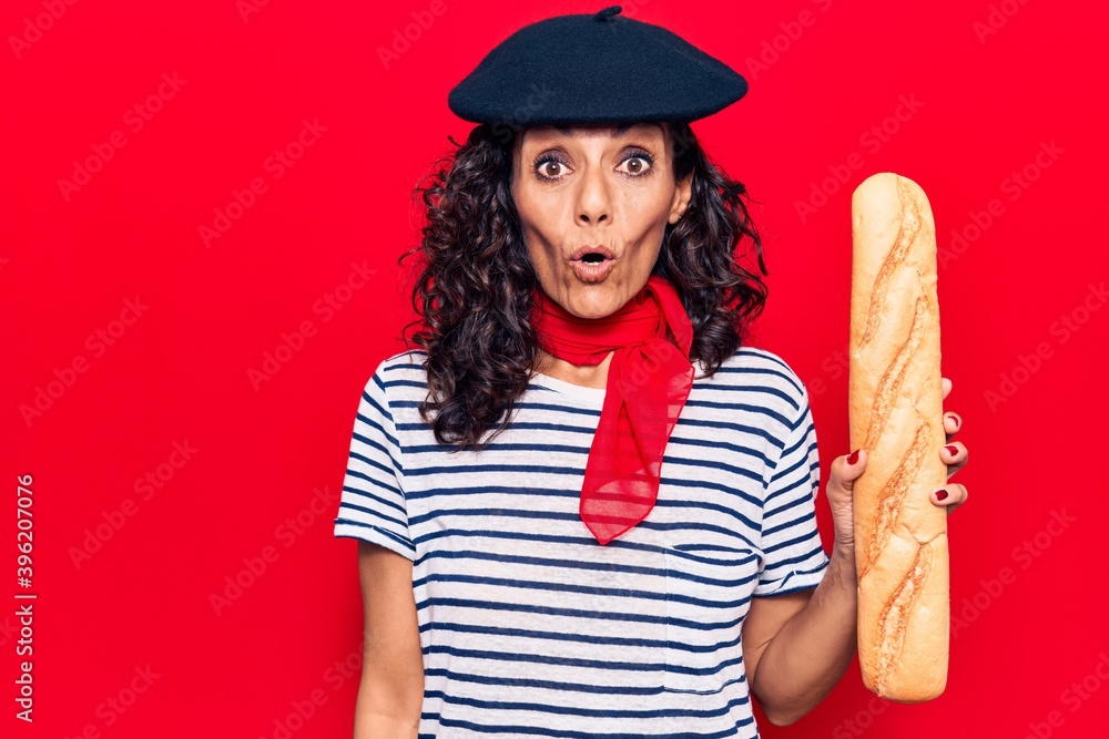 Middle age beautiful woman wearing french beret holding baguette scared and amazed with open mouth for surprise, disbelief face Middle age beautiful woman wearing french beret holding baguette scared and amazed with open mouth for surprise, disbelief face