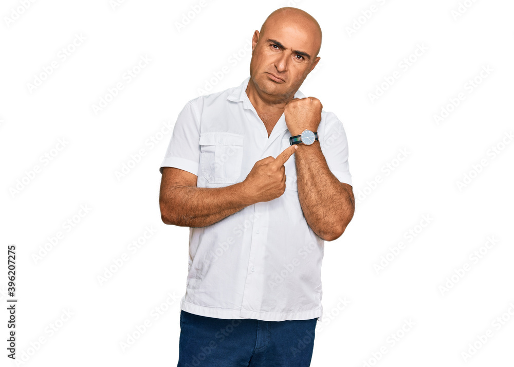 Mature middle east man with mustache wearing casual white shirt in hurry pointing to watch time, impatience, looking at the camera with relaxed expression Mature middle east man with mustache wearing casual white shirt in hurry pointing to watch time, impatience, looking at the camera with relaxed expression
