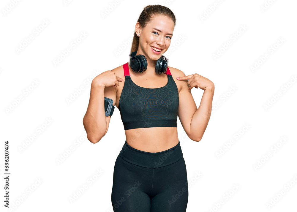 Beautiful blonde woman wearing gym clothes and using headphones looking confident with smile on face, pointing oneself with fingers proud and happy. Beautiful blonde woman wearing gym clothes and using headphones looking confident with smile on face, pointing oneself with fingers proud and happy.