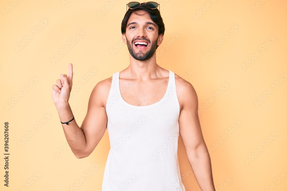 Handsome hispanic man wearing summer look and sunglasses showing and pointing up with finger number one while smiling confident and happy. Handsome hispanic man wearing summer look and sunglasses showing and pointing up with finger number one while smiling confident and happy.