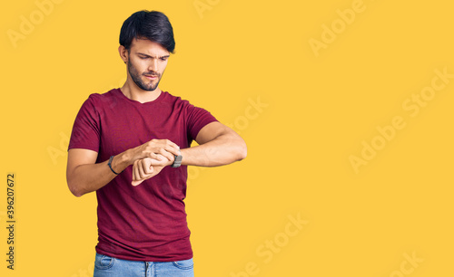 Handsome hispanic man wearing casual clothes checking the time on wrist watch, relaxed and confident