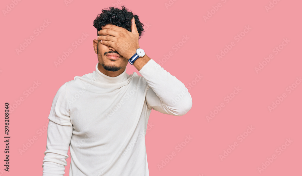 Young arab man wearing casual winter sweater covering eyes with hand, looking serious and sad. sightless, hiding and rejection concept Young arab man wearing casual winter sweater covering eyes with hand, looking serious and sad. sightless, hiding and rejection concept