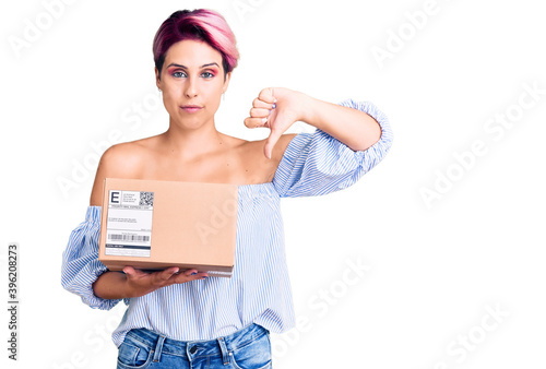 Young beautiful woman with pink hair holding delivery package with angry face  negative sign showing dislike with thumbs down  rejection concept