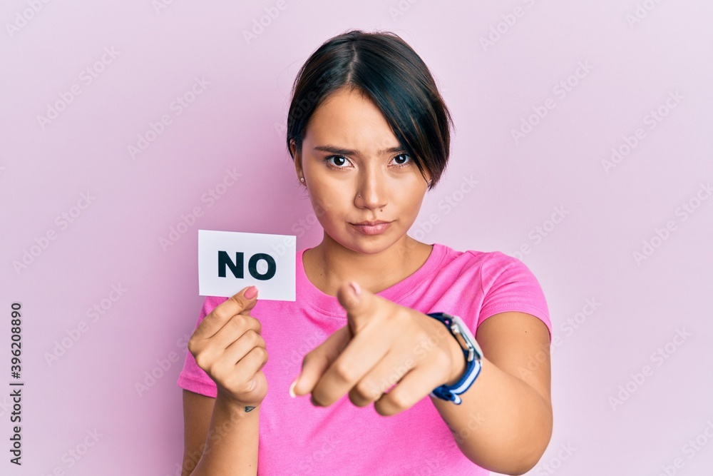 Beautiful young woman with short hair holding no word message pointing with finger to the camera and to you, confident gesture looking serious Beautiful young woman with short hair holding no word message pointing with finger to the camera and to you, confident gesture looking serious