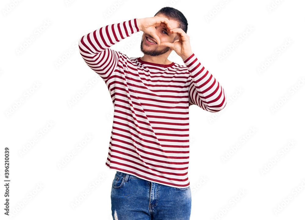 Young handsome man wearing striped sweater doing heart shape with hand and fingers smiling looking through sign Young handsome man wearing striped sweater doing heart shape with hand and fingers smiling looking through sign