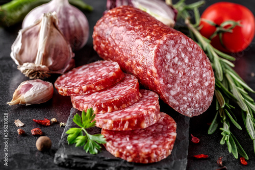 Traditional smoked salami sausage with spices.Salami sausage slices on a black chopping Board. Dark background.