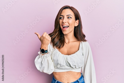 Young brunette woman wearing casual clothes over pink pointing thumb up to the side smiling happy with open mouth © Krakenimages.com