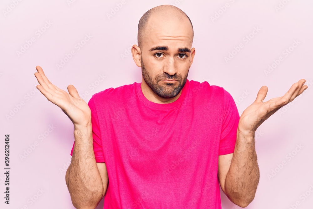 Naklejka premium Young handsome bald man wearing casual t shirt clueless and confused with open arms, no idea and doubtful face.