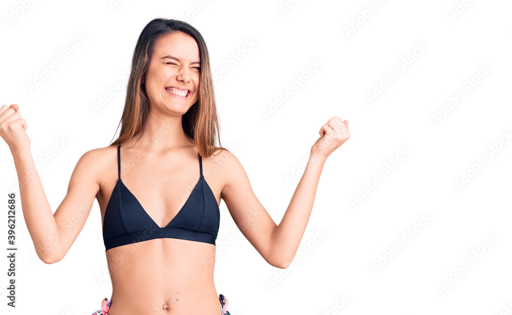Young beautiful girl wearing bikini very happy and excited doing winner gesture with arms raised, smiling and screaming for success. celebration concept. Young beautiful girl wearing bikini very happy and excited doing winner gesture with arms raised, smiling and screaming for success. celebration concept.