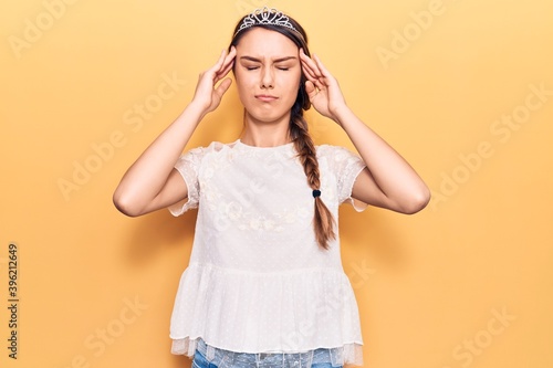 Young beautiful girl wearing crown princess with hand on head, headache because stress. suffering migraine.