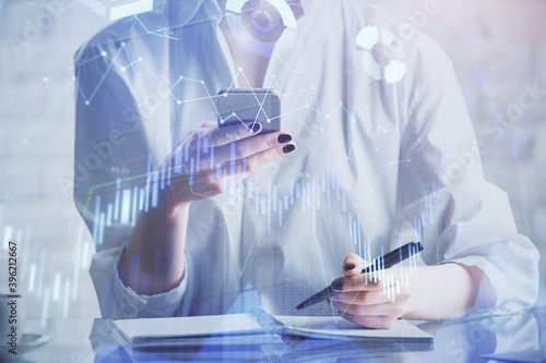 Double exposure of forex chart sketch hologram and woman holding and using a mobile device. Financial market concept.