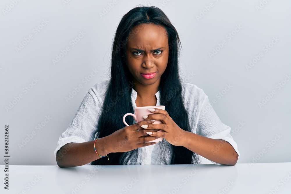 Young african woman drinking a cup coffee skeptic and nervous, frowning upset because of problem. negative person. Young african woman drinking a cup coffee skeptic and nervous, frowning upset because of problem. negative person.