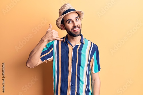 Young handsome man with beard wearing summer hat and shirt smiling doing phone gesture with hand and fingers like talking on the telephone. communicating concepts.