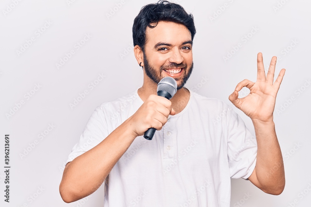 Young hispanic man singing song using microphone doing ok sign with fingers, smiling friendly gesturing excellent symbol Young hispanic man singing song using microphone doing ok sign with fingers, smiling friendly gesturing excellent symbol
